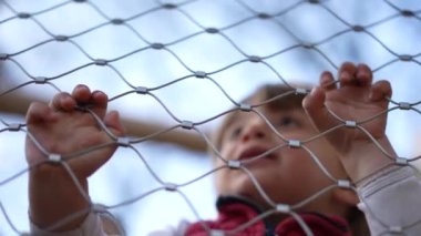 Küçük çocuk oyun bahçesindeki metal çitlere yaslanıyor.