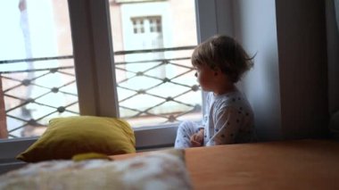 Küçük çocuk pencerenin kenarında oturuyor ve sabahları dışarı bakıyor.