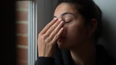 Yorgun bir kadın pencerenin kenarında otururken acı çeker. Duygusal ızdırap