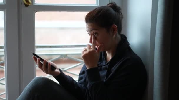 Kobieta Pocierając Oczy Twarz Ręką Trzymając Telefon Komórkowy Przez Okno — Wideo stockowe