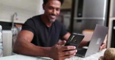 Akıllı telefon ve dizüstü bilgisayar kullanarak evde çalışan Afrikalı bir adam