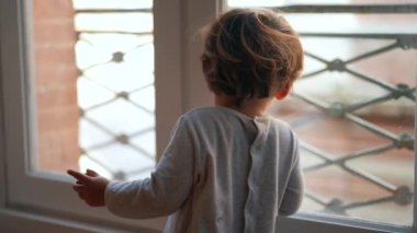 Pencere kenarında oturan küçük çocuk dışarı bakıyor. Çocuk sabah oturur.