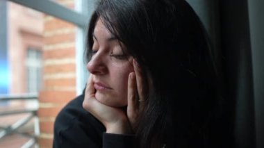 Düşünceli melankolik kadın pencereden dışarı bakıyor.
