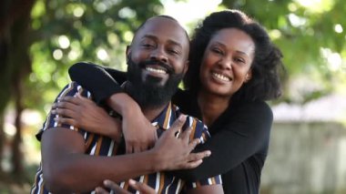 Afrikalı çift kameraya bakarak kucaklaşır. Siyahi farklı ortaklar parkta sarılıyor