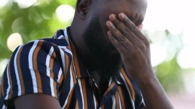 Üzgün Afrikalı bir adam hayal kırıklığı ve endişeyle yüzünü eliyle kapatıyor.