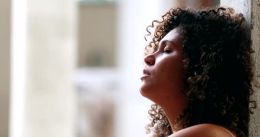 Düşünceli bir kadın duvara yaslanmış, gözleri kapalı düşünüyor.