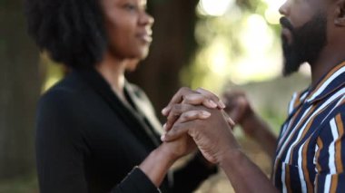 Siyah çift el ele tutuşup güneş parkında öpüşüyor.