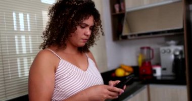 Ciddi dürüst bir kadın cep telefonunu elinde tutuyor ve ekranda mutfağa bakıyor.
