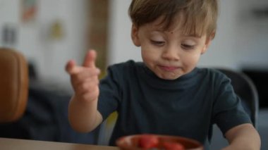 Küçük çocuk kaseden meyve topluyor.