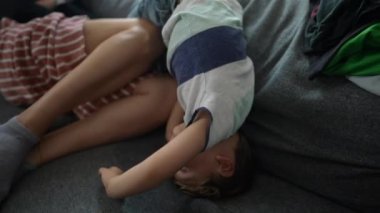 Küçük çocuk evdeki kanepede baş aşağı oyun oynuyor.