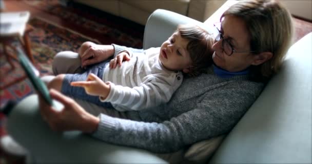 Kanepede Otururken Tablet Kullanırken Kucağında Bebek Tutan Büyük Anne — Stok video