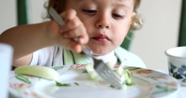 Sağlıklı sebzeleri çatalla yiyen çocuk, yakından bakan bebek çatal kullanmayı öğrenerek yemek yiyor.