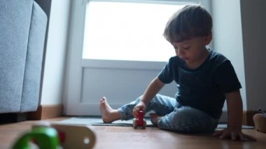 Küçük çocuk ev zemininde geleneksel tahta araba oyuncaklarıyla oynuyor.