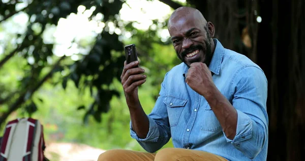 African man celebrating achievement holding cellphone