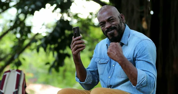 African man celebrating achievement holding cellphone