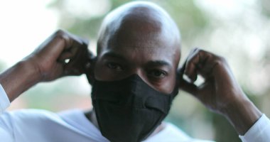 Afrikalı bir adam kameraya bakarken maske takıyor.