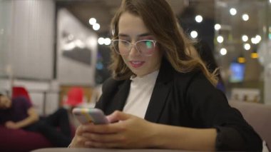 Geceleri gülümseyen cep telefonu cihazına bakan mutlu genç bir kadın. Yetişkin milenyum kızı akıllı telefondan internette geziniyor.