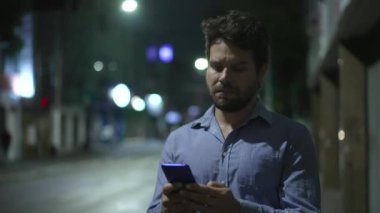 Şehir merkezinde gece yürürken cep telefonu ekranına bakan genç bir adam. Akşamları yürüyen kişi elinde telefonla yürüyor.