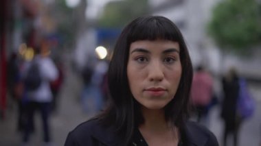 Sokakta dikilen Latin kökenli genç bir kadın. Güney Amerikalı Latin Brezilyalı kadın kameraya ciddi bir ifadeyle bakıyor.