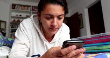 Yatakta yatan cep telefonu cihazına mesaj yazan kadın.