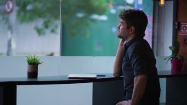 Pencere kenarında oturmuş kaldırımdaki şehir sokağına bakan dalgın genç adam. Düşünceli erkek hayal kuruyor.