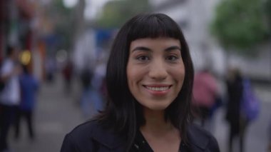 Sokakta gülümseyen mutlu İspanyol genç kadın. Bir Güney Amerikalı Latin yetişkin kız fotoğraf çekimine yakından bakıyor.