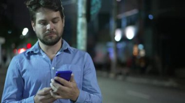Gece sokakta yürürken telefonu kullanan genç bir adam. Akıllı telefon aygıtı ekranına bakarak şehir kaldırımında mesaj yazan kişi