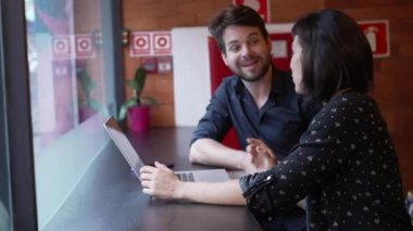 Dizüstü bilgisayarın önünde pencere kenarına oturmuş iş hakkında konuşan iki genç insan. İş adamı ve kadın planlama ve strateji hakkında konuşuyor.
