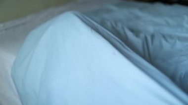 Küçük çocuk yatağa tırmanıyor, çocuk çarşaflarla oynuyor.