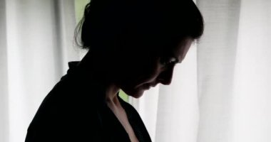 Siluet kadın pencerenin yanında duran cep telefonu içeriğine bakıyor.