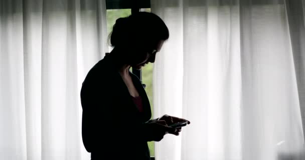 Silhouette Frau Schaut Auf Handy Leseinhalt Fenster Stehen — Stockvideo