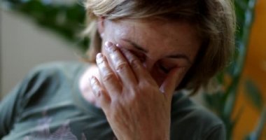 Yorgun yaşlı kadın, elleriyle gözlerini ve yüzünü ovuşturuyor.