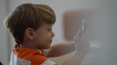 Bir çocuk elinde akıllı bir telefonla ekrandaki çocuğa telefon teknolojisi kullanarak bakıyor.