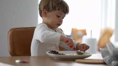 Yeni yürümeye başlayan çocuk, öğle yemeği sırasında çatal bıçak kullanarak tek başına yemek yiyor.