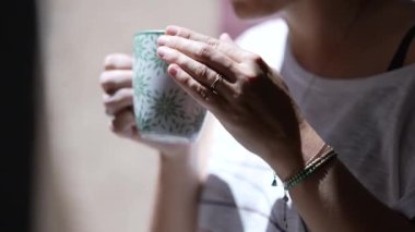 Çayı yudumlayan kadın kahve içiyor ve dışarı bakıyor.