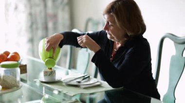 Sabahları kahvaltı masasında kendine kahve servisi yapan sıradan bir kadın pencereden dışarı bakıyor.