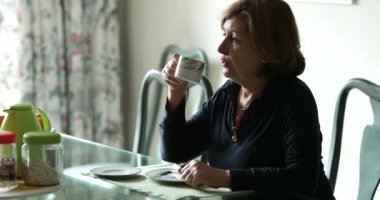 Düşünceli, samimi, meditasyon yapan yaşlı bir kadın sabahları kahve içiyor. Yaşlı bir kadının sabah sıcak içecek içtiği otantik gerçek hayat sahnesi.