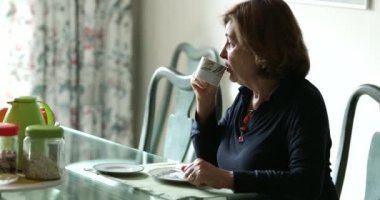 Sabahleyin kahvaltı masasında, soğuk bir şeyler içmek için üfleyen yaşlı bir kadın.