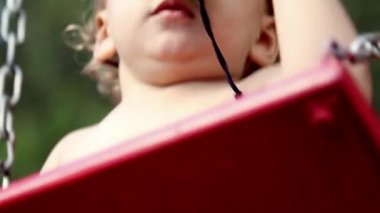 Çocuk bahçesinde salıncakta sallanan ve elinde dürbünle oynayan şirin bir bebek.