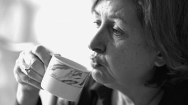 Sıcak kahveyi siyah beyaz üfleyen sıradan bir yaşlı kadın.