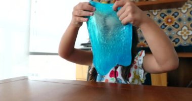 Little girl playing with slimy plasticine creating a bubble with blue slime