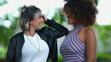 Dışarıda gülümseyen iki farklı kadın.