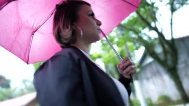 Yağmurlu bir günde elinde pembe şemsiyeyle dışarıda yürüyen genç bir kadın.