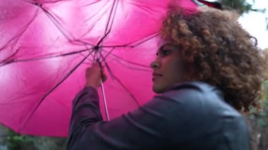 Yağmurlu bir günde elinde pembe şemsiyeyle dışarıda yürüyen genç bir kadın.