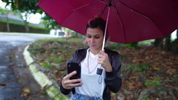 Jonge Vrouw Met Paraplu Kijken Naar Mobiele Telefoon Apparaat Staan — Stockvideo