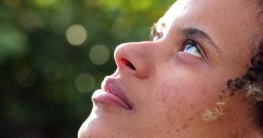 Tatmin olmuş genç siyahi kadın gülümseyen gökyüzüne bakıyor.