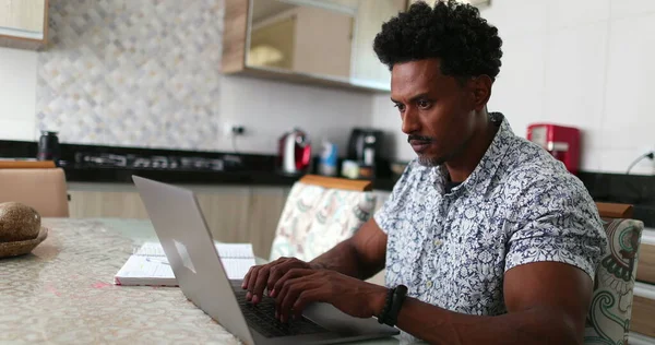 Black African man using laptop computer at home kitchen table