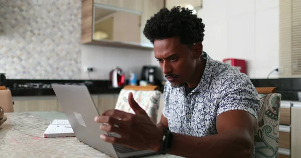 Black African man using laptop computer at home kitchen table