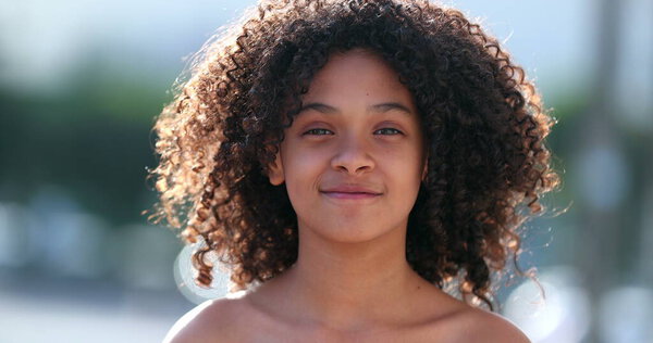 African preteen girl smiling at camera. Black child standing outside with curly hair