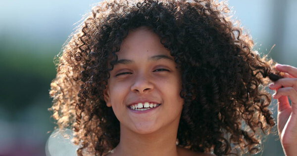 African preteen girl smiling at camera. Black child standing outside with curly hair